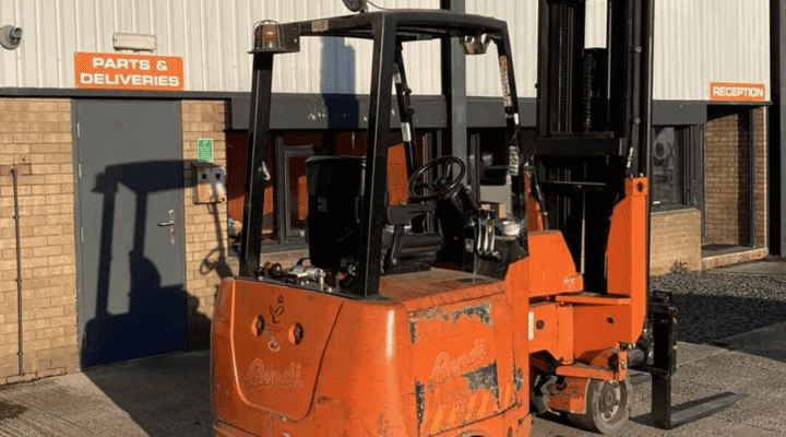 A bright orange industrial forklift positioned outside a warehouse with parts and deliveries signage.