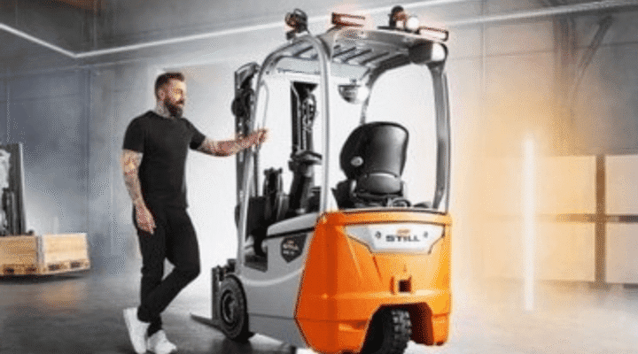A person standing next to a modern electric forklift in an industrial warehouse environment.