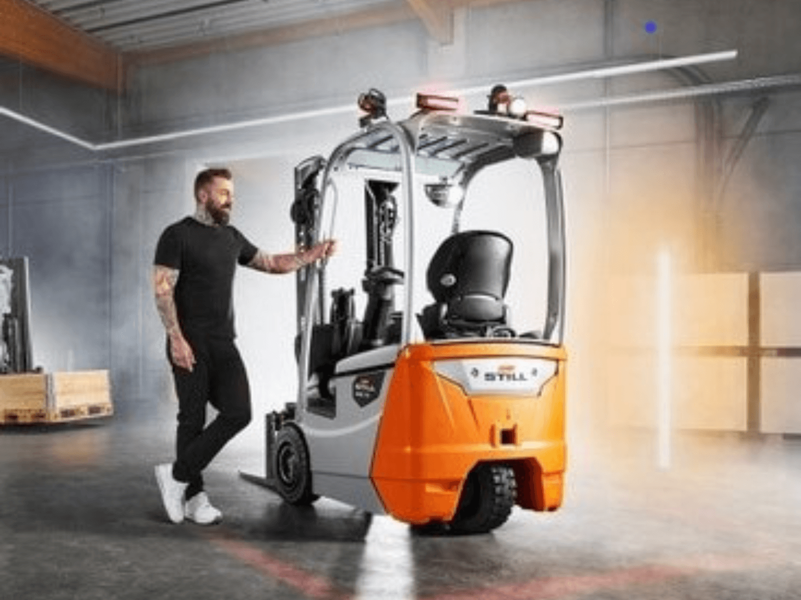 A person standing next to a modern electric forklift in an industrial warehouse environment.