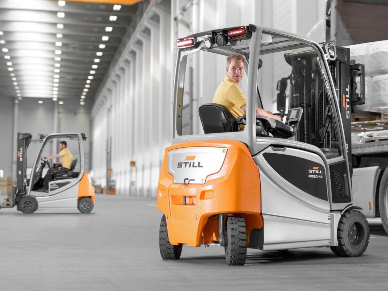 Forklift Operating in Warehouse Environment A worker driving a STILL forklift in a spacious warehouse with another forklift in the background.