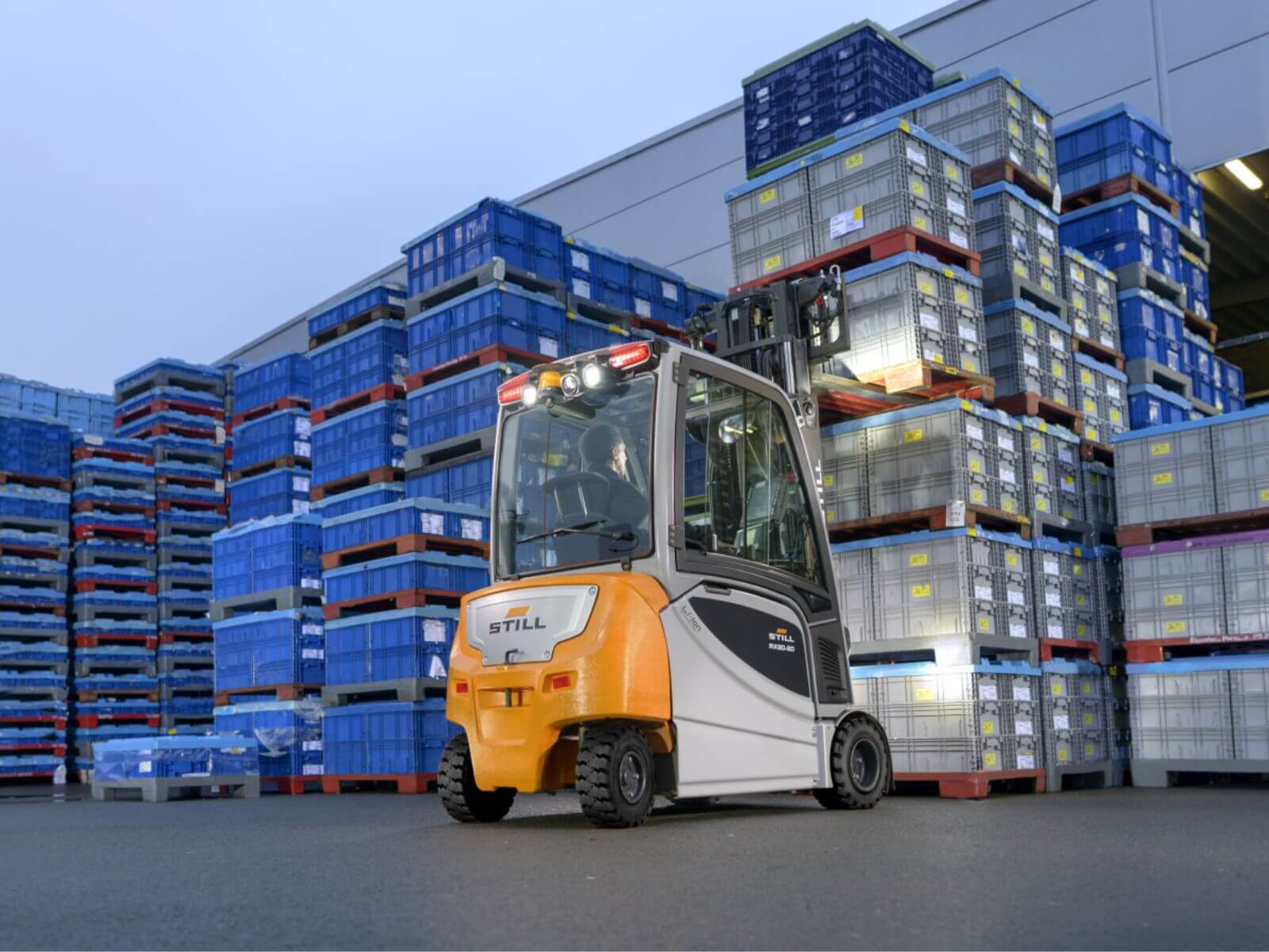 Electric Forklift in Warehouse with Stacked Pallets An electric forklift positioned in front of tall stacks of blue and gray pallets in a warehouse setting, showcasing industrial logistics equipment.