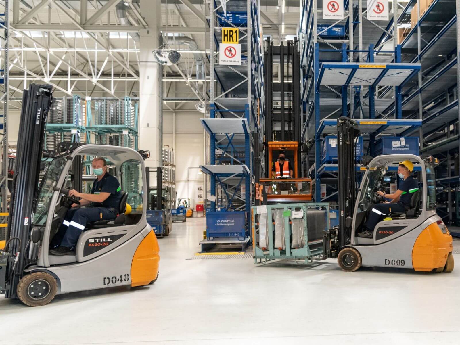 Warehouse Operations with Forklifts Two operators using forklifts in a large warehouse setting near storage racks.
