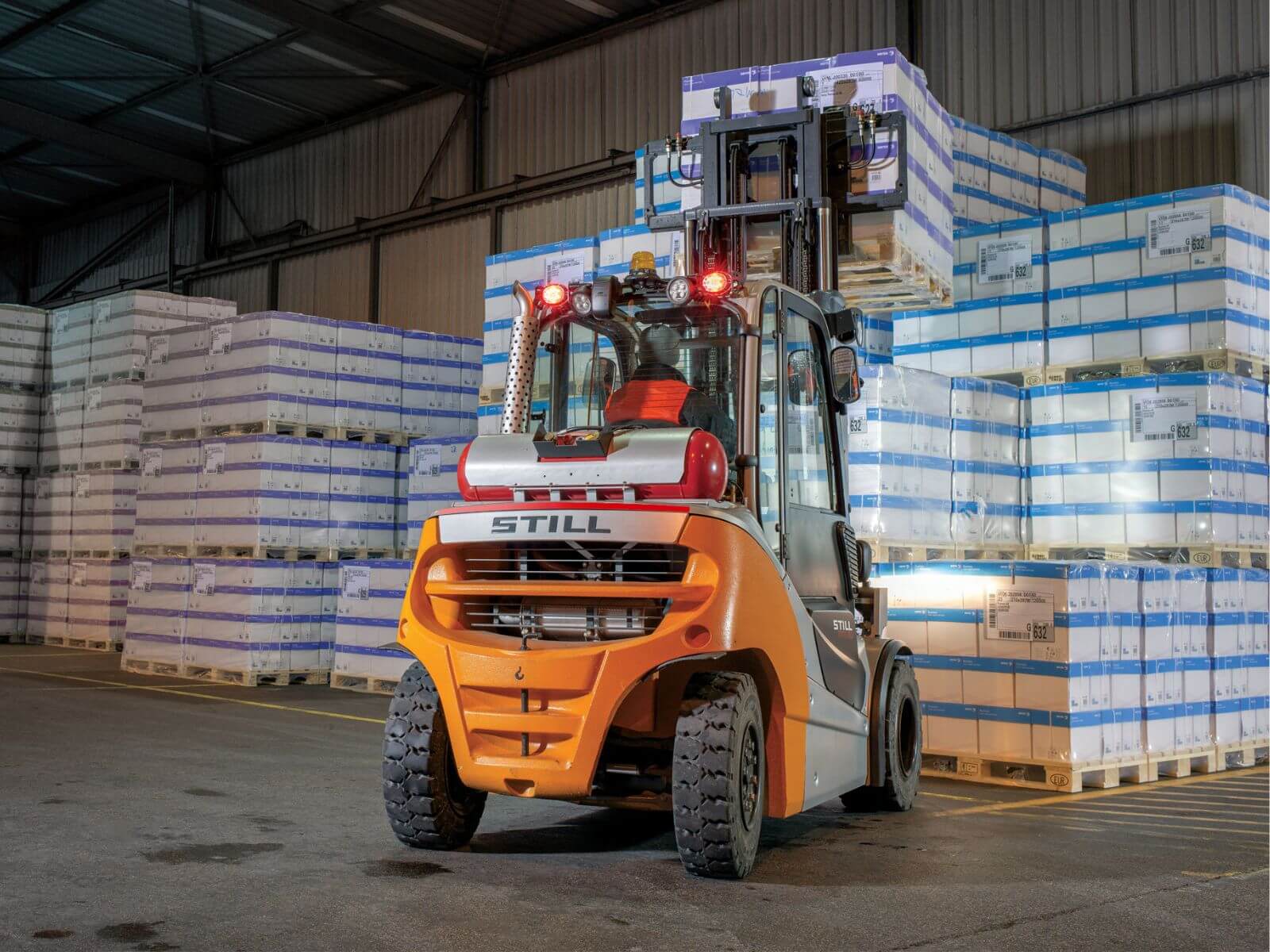 Warehouse Forklift Handling Pallets of Goods A STILL forklift in a warehouse lifting pallets stacked with products, showcasing efficient material handling operations.