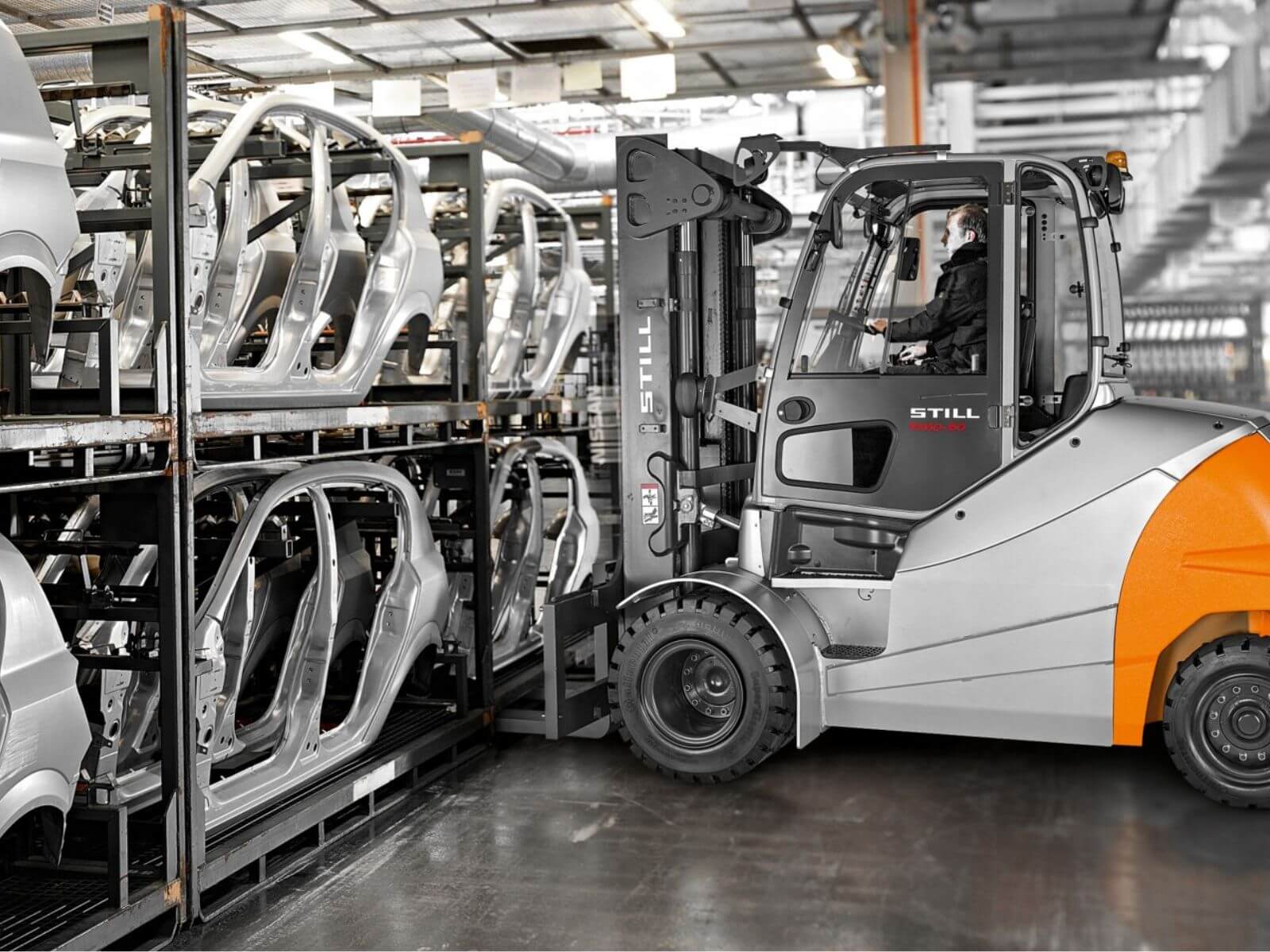 Industrial Forklift in Car Manufacturing Facility A forklift maneuvering between racks of car frames in a manufacturing warehouse.