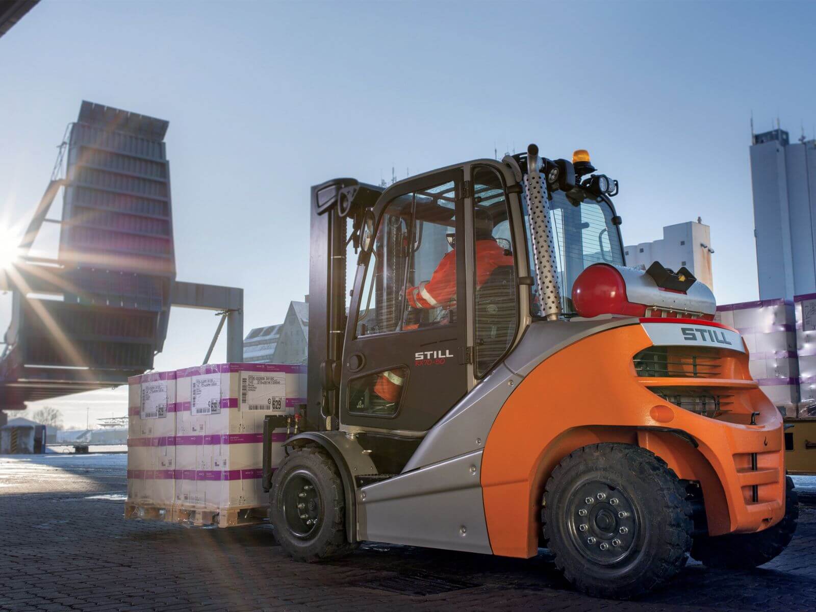 Industrial Forklift in Action at a Warehouse A forklift maneuvering pallets at a loading dock with sunlight in the background.