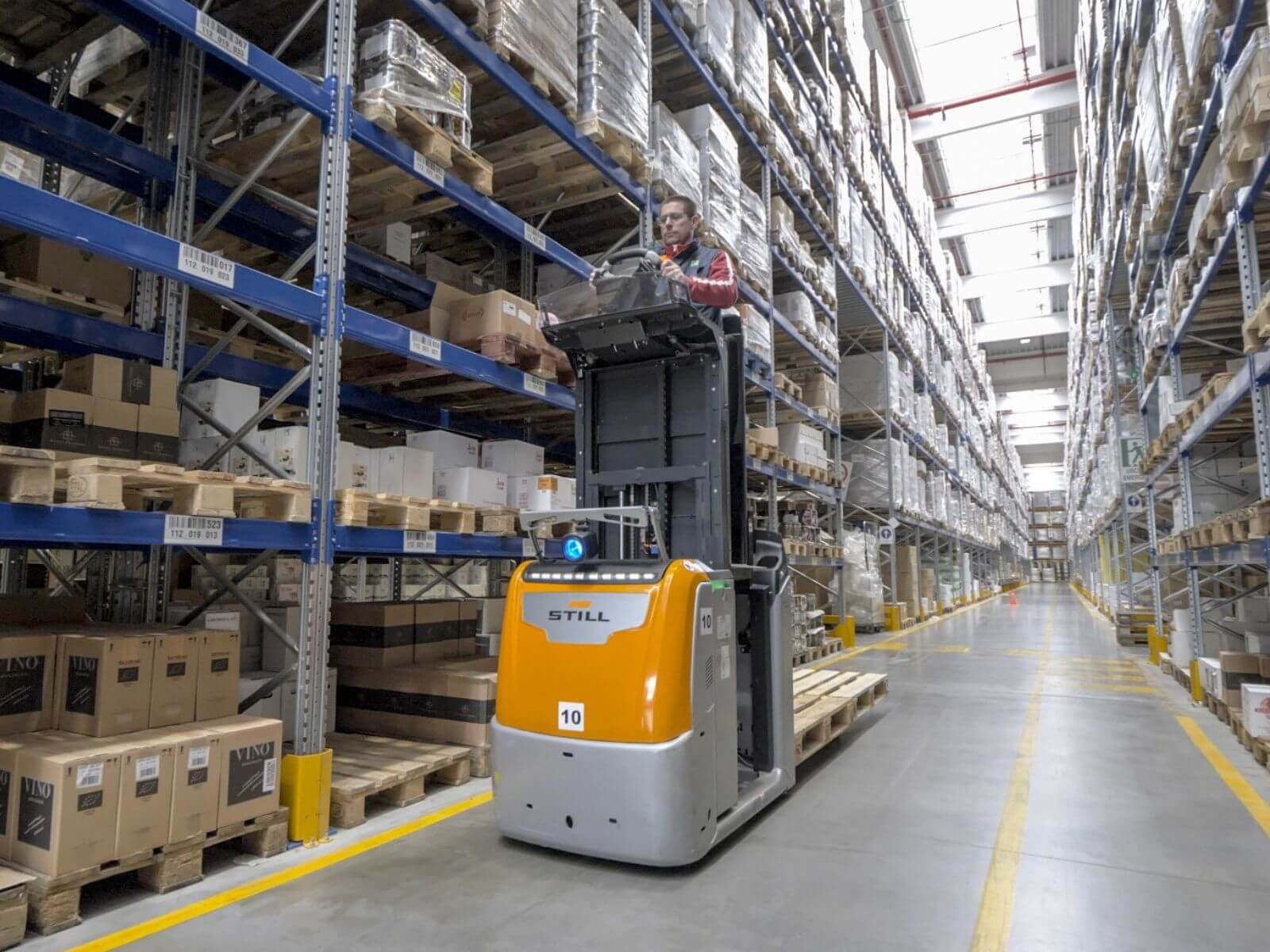 Warehouse Worker Operating a Forklift in a Storage Facility A warehouse worker using a forklift to reach elevated shelves in a well-organized storage facility with stacked boxes.