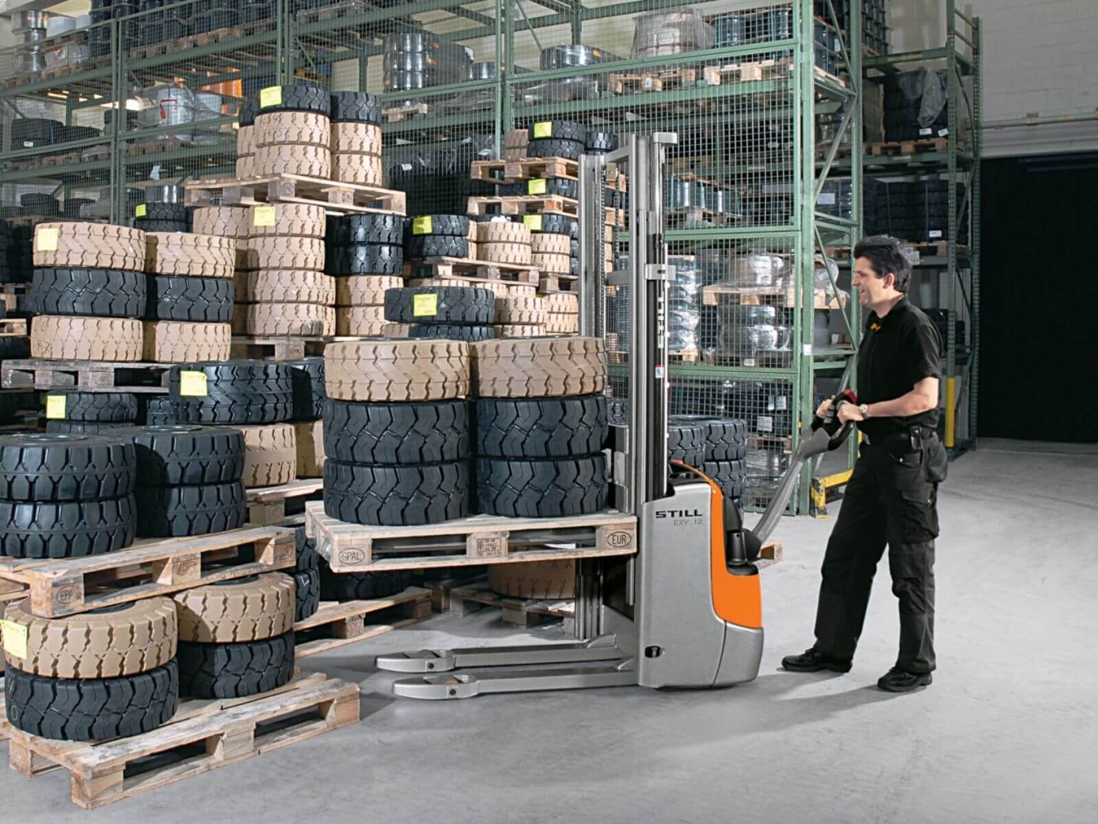 Forklift in Warehouse with Stack of Tires A warehouse worker operating a forklift next to stacks of tires on wooden pallets.