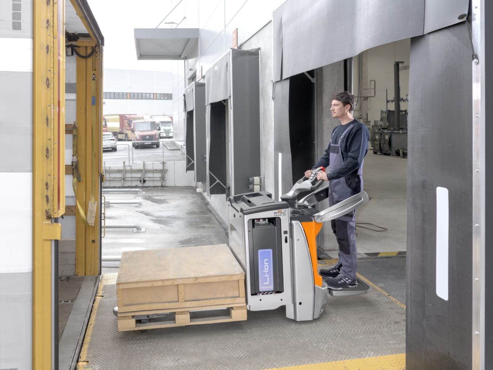 A worker using a pallet jack to move a wooden pallet in a warehouse setting.