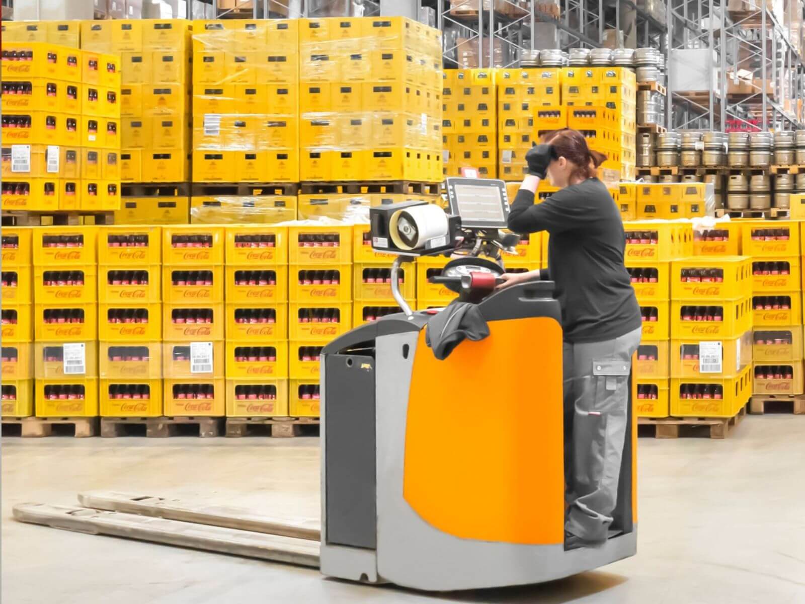 A warehouse worker using a forklift in front of stacked yellow crates.