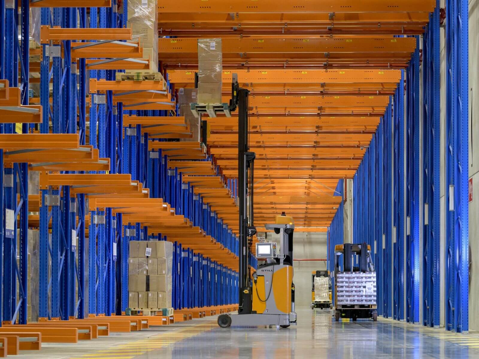 Modern Warehouse Interior with Automated Forklifts A spacious warehouse with blue steel shelving and automated forklifts navigating the aisles.