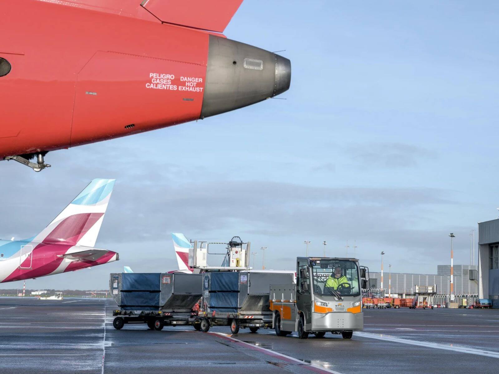 Airport Ground Operations with Aircraft and Baggage Vehicles A close-up view of an aircraft's engine with a ground handling bus and baggage carts at an airport terminal.