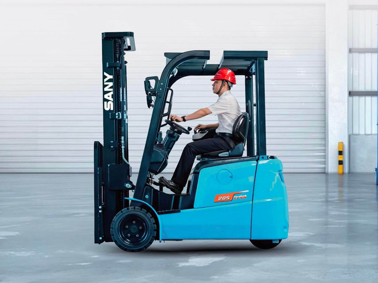 A worker operating a blue electric forklift inside a warehouse with safety gear.