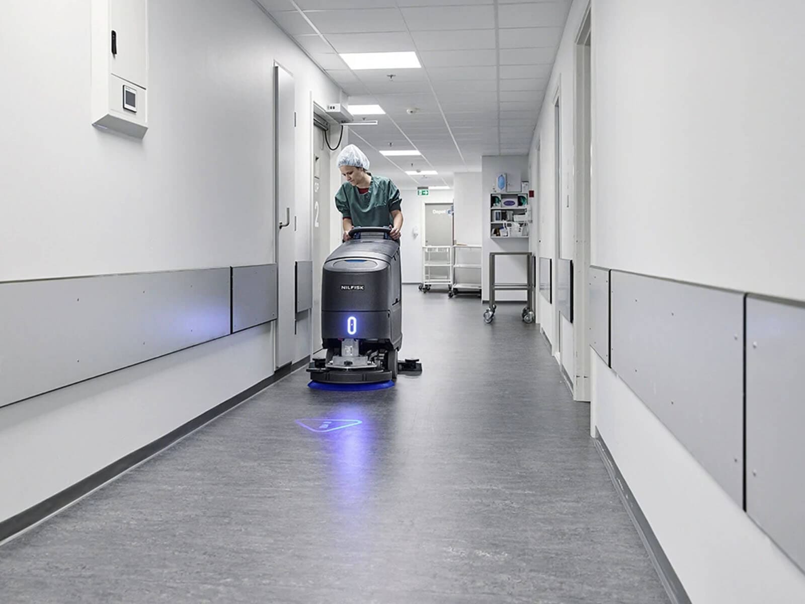 A healthcare worker using a professional cleaning machine in a hospital corridor