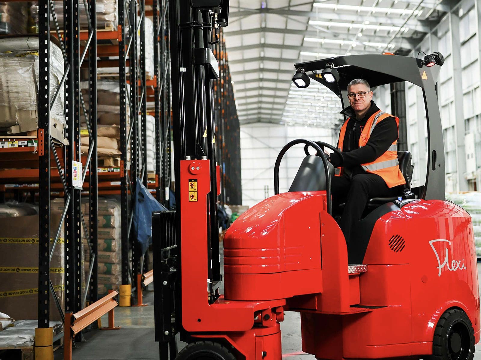 A person operating a red forklift in a warehouse setting, surrounded by shelves of goods.